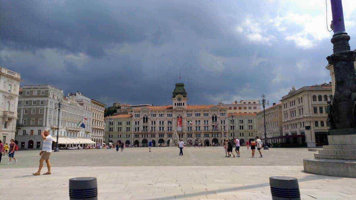 Cappello centrale Piazza Unità d'Italia a Trieste con edifici storici e cielo nuvoloso.