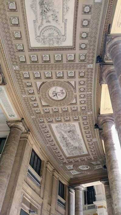 Dettaglio dell'architettura classica con soffitto decorato e colonne in marmo, ambientazione storica e artistica ricca di dettagli ornamentali e sculture.