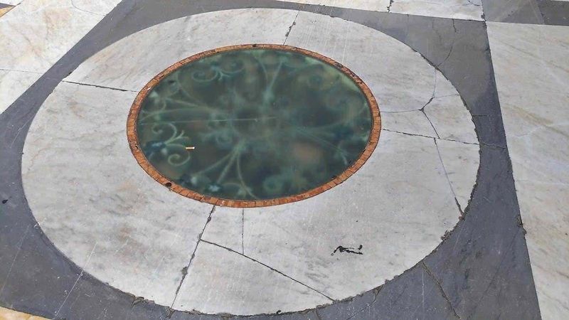 Galleria Umberto I Napoli regno dei sciuscià 12 Vetolo ottagonale con vetro colorato e decorativo, installato in un pavimento in pietra con motivi geometrici in bianco, grigio e nero. Design artistico e dettagli architettonici eleganti.