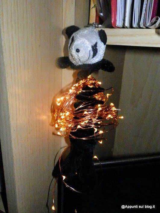 Peluche di panda con luci natalizie avvolte intorno a un tavolo in soggiorno, decorazione festiva per l'inverno e l'atmosfera natalizia.