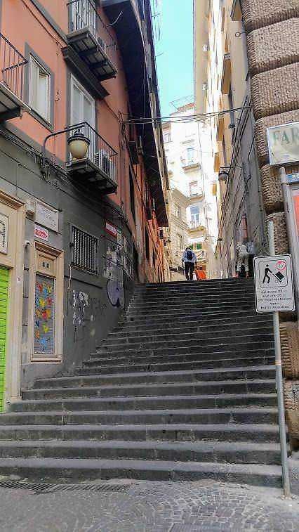 Napoli 12 siti tra arte, pizza e caffè espresso 18 Coppie di scale in zona urbana di Napoli con edifici storici, strada stretta e ringhiere di ferro, rappresentando un tipico scorcio cittadino.