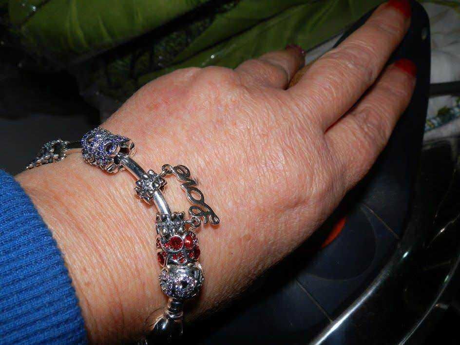 Bracciale in argento con charms a forma di animali e piante, indossato su una mano femminile con unghie rosse.