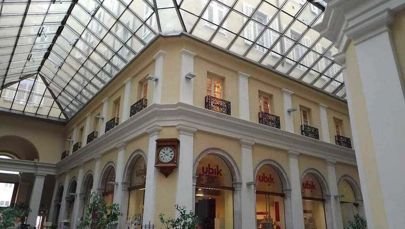 Architettura storica con galleria in vetro e attico, interni eleganti dell'edificio con negozi e orologio, ambiente raffinato e luminoso, immagini di design e decorazioni per blog di stile e architettura.