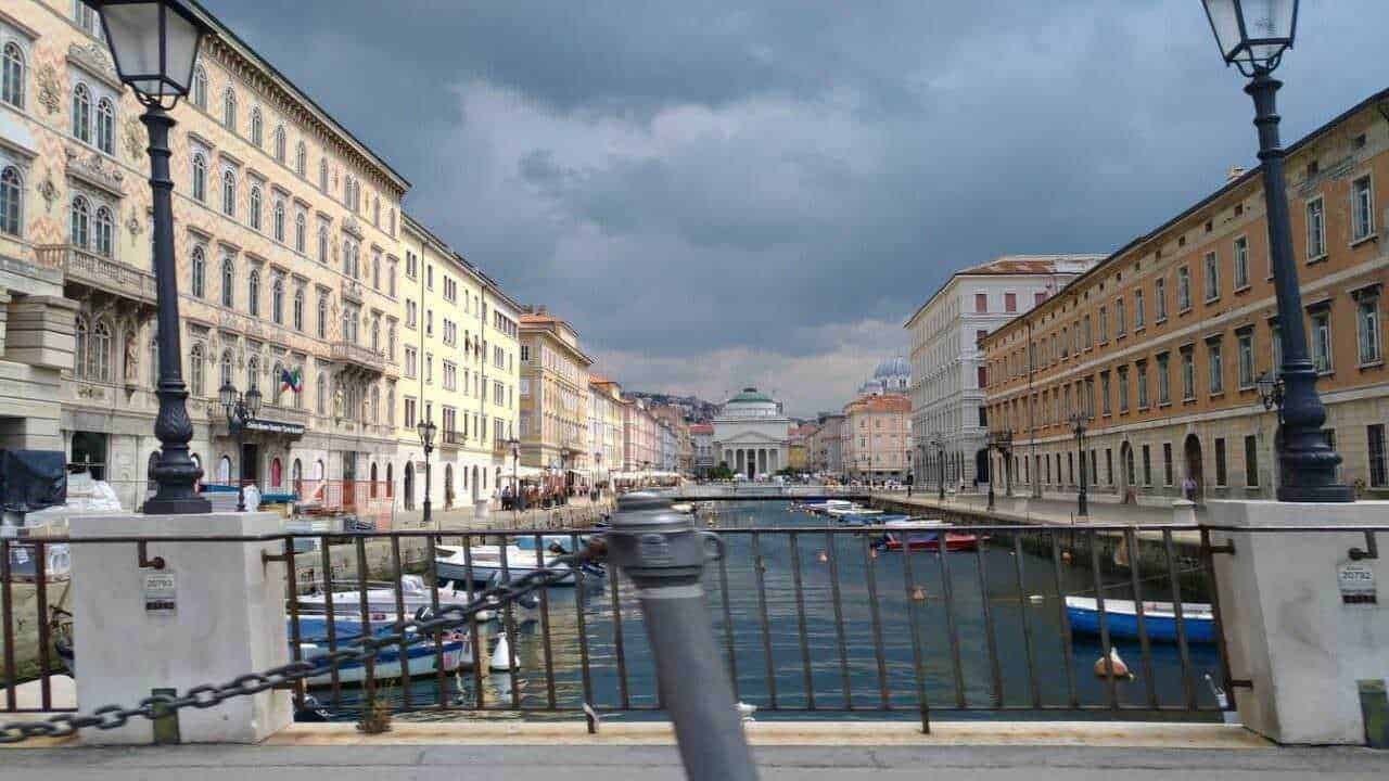 Vicolo con vista sul Canale di Genova, con edifici storici e barche attraccate, sotto un cielo nuvoloso.