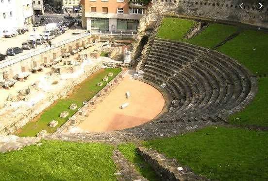 Antico teatro romano di Napoli con sedili in pietra e arena, esempio di archeologia e storia antica, visitabile e affacciata sulla città moderna.