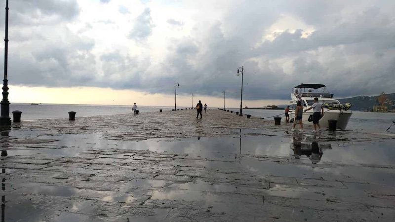 Trieste asburgica, 9 siti da raggiungere a piedi 11 Passerella sul porto di mare con barche e persone che passeggiano, cielo nuvoloso, atmosfera marina e rilassante, ideale per blog di viaggi e destinazioni estive.
