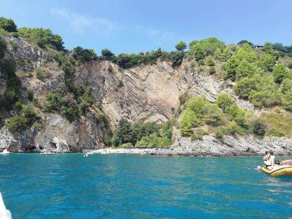 Scogliera e mare blu in Liguria, Italia, con vegetazione verde e barche in acqua, paesaggio naturale e spettacolare destinazione turistica per relax e avventure acquatiche.