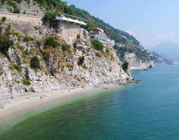 Spiaggia sul mare con scogliere e case sul promontorio, vista panoramica sulla costa mediterranea, viaggio in Italia, destinazioni turistiche, relax al mare, vacanze estive.