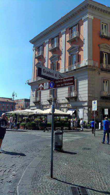 Stazione di Piazza del Duomo a Milano con negozi e caffè all'aperto, civico storico e traffico pedonale intenso. Atmosfera urbana vivace e architettura classica italiana.