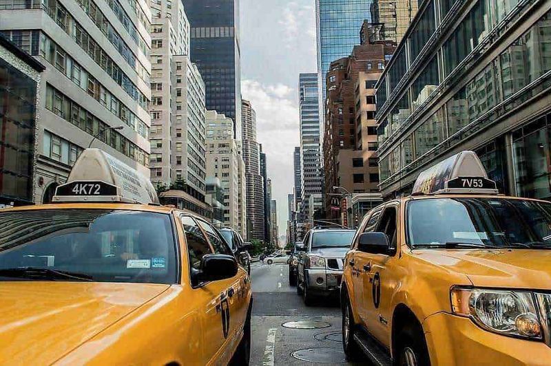 Storia del Taxi: dall'Hansom cab dell'Ottocento all'era moderna 6 Yellow taxis in New York City bustling street with tall skyscrapers, urban transportation, city life, and iconic yellow cabs.
