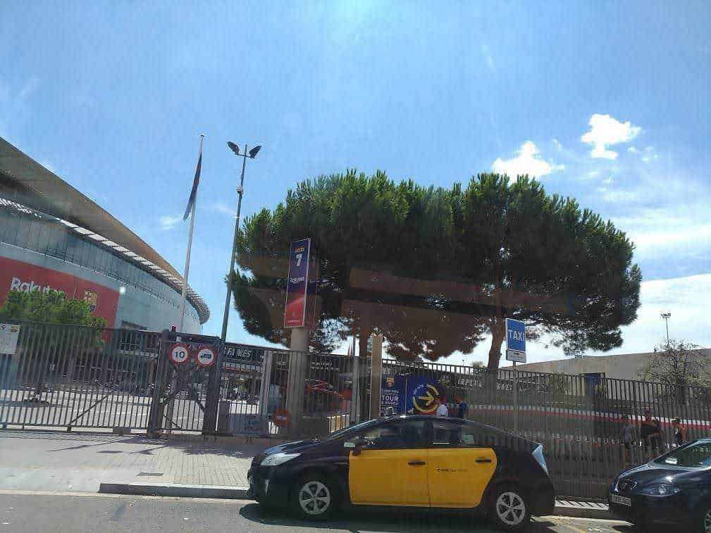 Hansom cab: Un grande stadio con albero ornamentale e auto gialla parcheggiata lungo la strada, in un giorno di sole soleggiato.