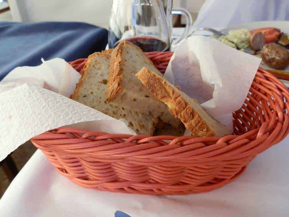 Pane casereccio in cestino con vino rosso e piatto di carne, stile italiano.
