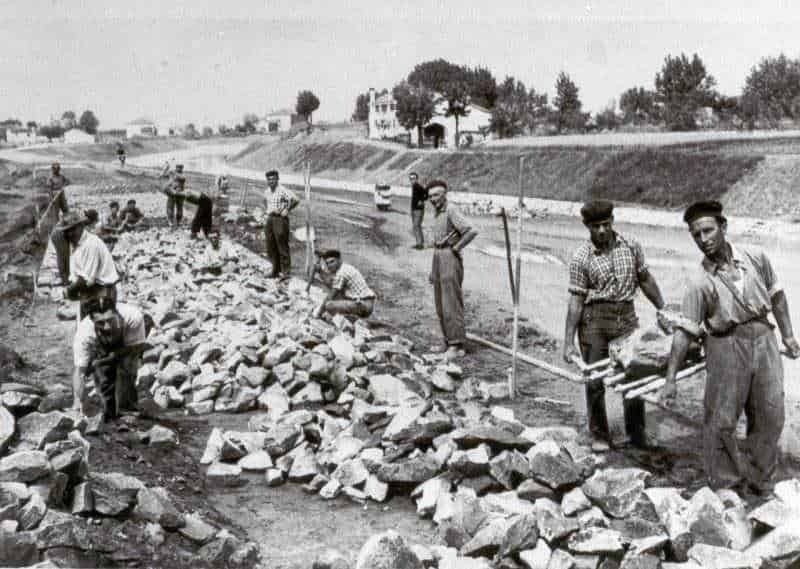 Cantiere di lavoro con operai che posano pietre per la costruzione di una strada, immagine storica di lavori pubblici in Italia.