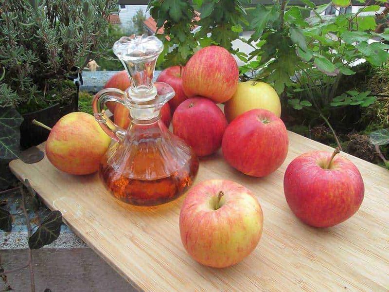 Iperidrosi facciale cause e rimedi sudorazione eccessiva 4 Mele rosse e gialle con bottiglia di sidro di mele artigianale su un tavolo di legno in giardino.