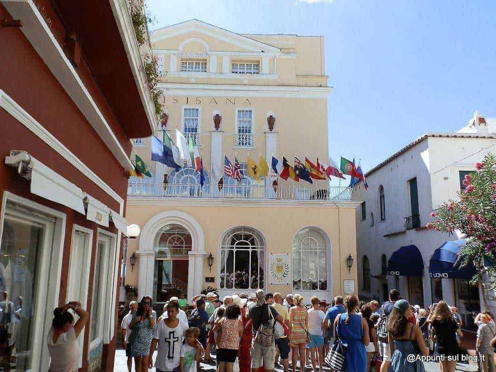 Folla di turisti in Piazza a Capri, con edifici storici e bandiere italiane e straniere