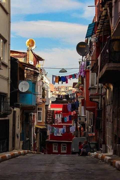 Lavandino in un vicolo stretto di quartiere urbano con panni stesi all'aperto e satellite sulla facciata degli edifici, cielo azzurro e nuvole, atmosfera quotidiana, vita di strada, edilizia storica, cultura urbana, appartamenti, zona residenziale, fotografia di strada.