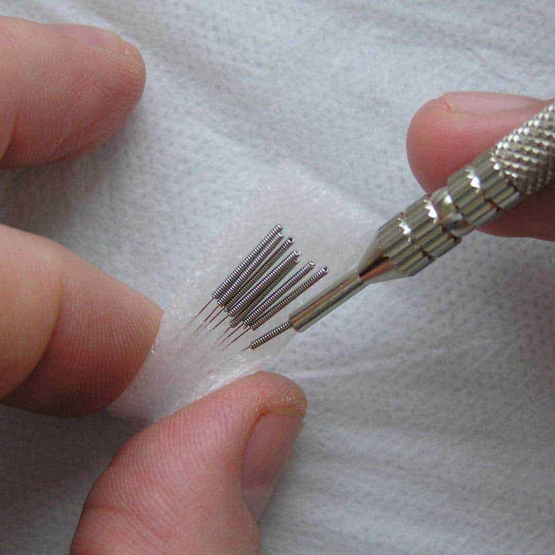 Piccole aghi e strumenti per trattamenti di microdermoabrasione o estetici, posati su un tessuto chiaro, utilizzati in procedure di cura della pelle o cosmetiche.