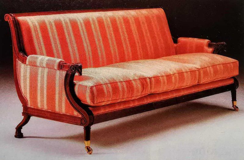 Arredo classico, conosci i 4 stili più famosi? 6 Antico divano in velluto rosso con dettagli in legno intagliato e ruote, stile classico ed elegante, perfetto per arredare un soggiorno di charme o un ambiente vintage.