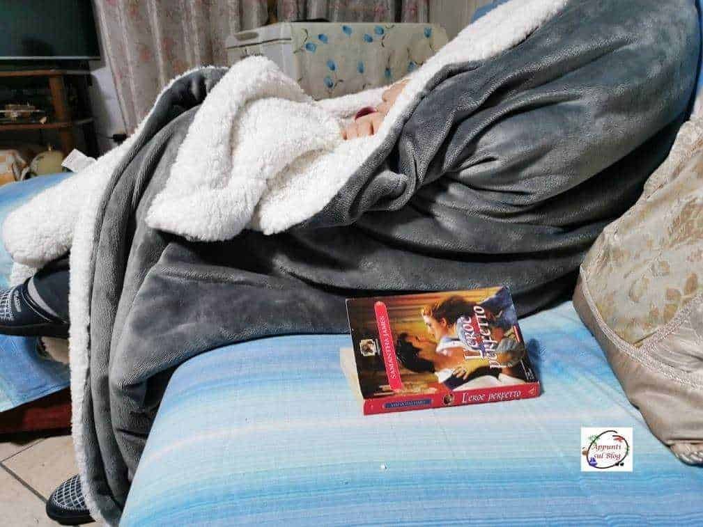 Sognatore sdraiato su un divano con coperta grigia e libro aperto, ambiente casalingo confortevole, atmosfera rilassante, ideale per leggere o riposare.