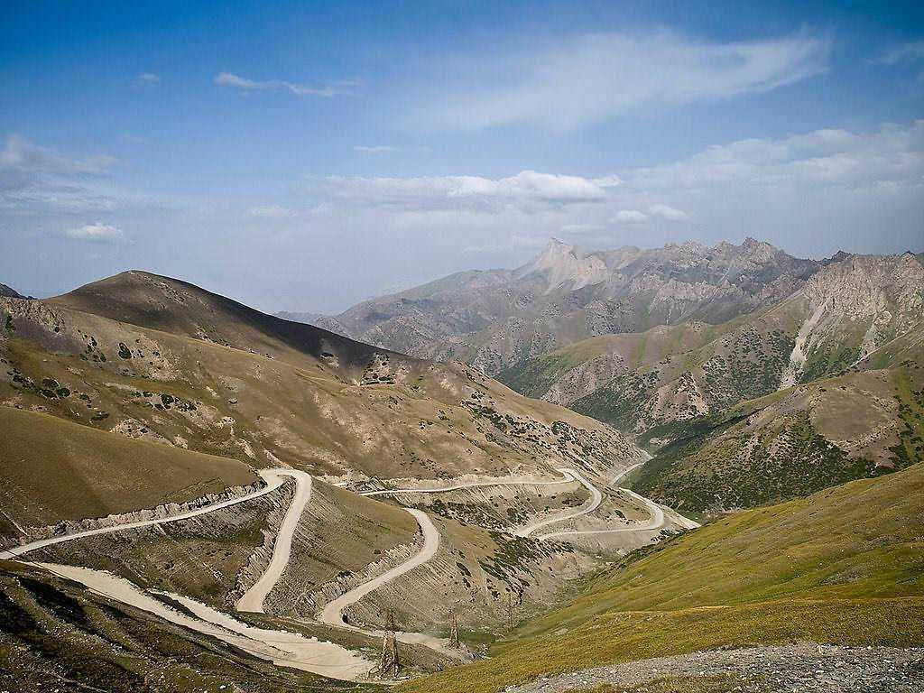 Strada di montagna con curve strette tra colline e montagne, paesaggio naturale, cielo nuvoloso, vista panoramica, escursioni in natura, viaggio e avventura.
