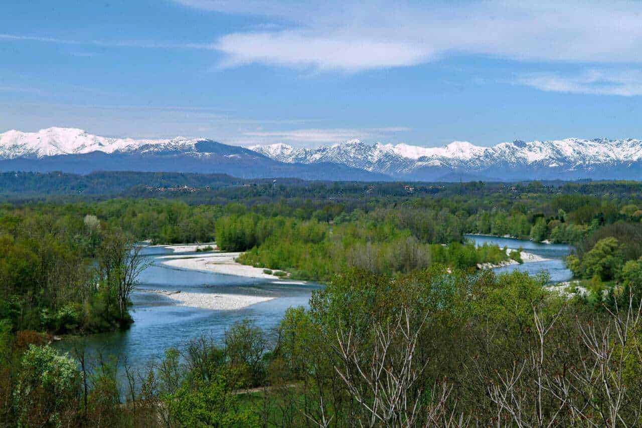 Fiume che attraversa una vasta area verde con montagne innevate sullo sfondo in una scena naturale e selvaggia.