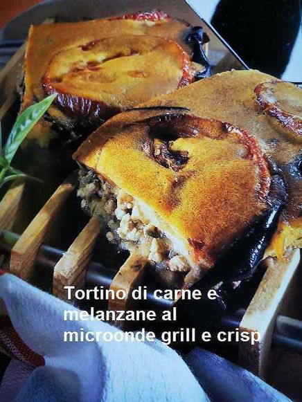 Tortino di carne e melanzane al microonde grill e crisp 3 Tortino di carne e melanzane cotto al microonde, con superficie dorata e croccante, servito su uno steamer di legno, ideale per un piatto saporito e veloce.
