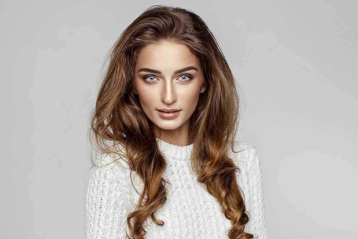 Capelli lunghi e mossi, bellezza naturale e trucco leggero, modello femminile in abbigliamento casual, sfondo grigio chiaro, stile moda e bellezza.