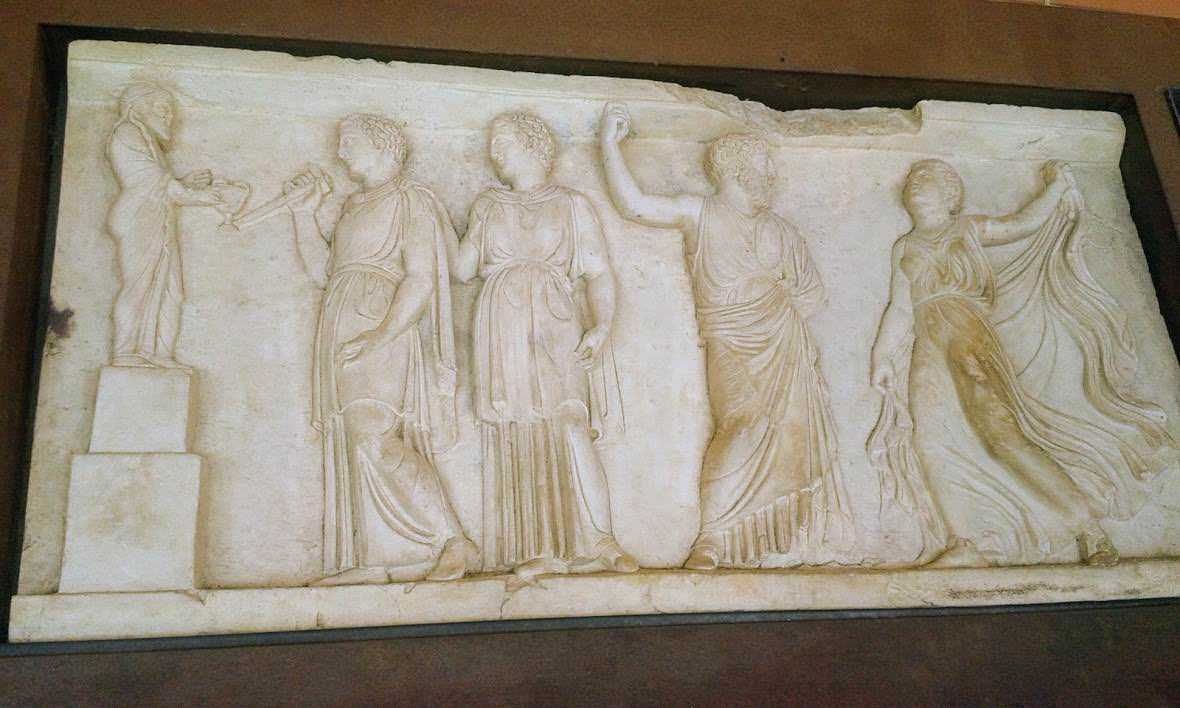 Carro scolpito in marmo con figure dell'antica Grecia, scena mitologica con divinità e figure femminili elegantemente vestite, dettaglio di arte classica, perfetta rappresentazione della scultura antica.