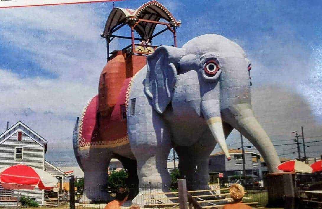 Elefante gigante di peluche colorato con struttura di bambù, decorato con stoffe colorate, in un parco giochi all'aperto, perfetto come attrazione turistica e simbolo di creatività in un ambiente familiare.