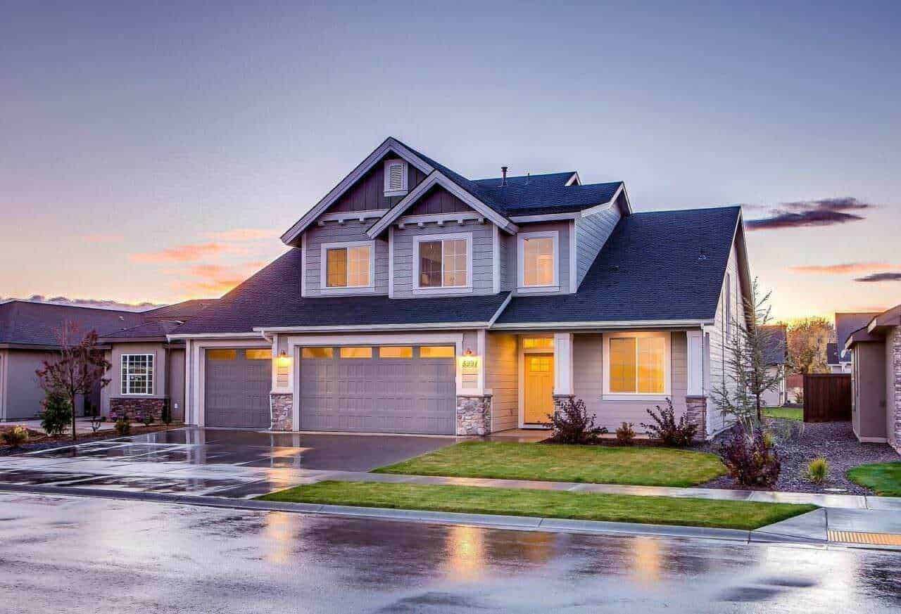 Elegante casa moderna con garage a doppia porta, illuminata dal tramonto, sotto un cielo sereno, in un quartiere residenziale ben curato.