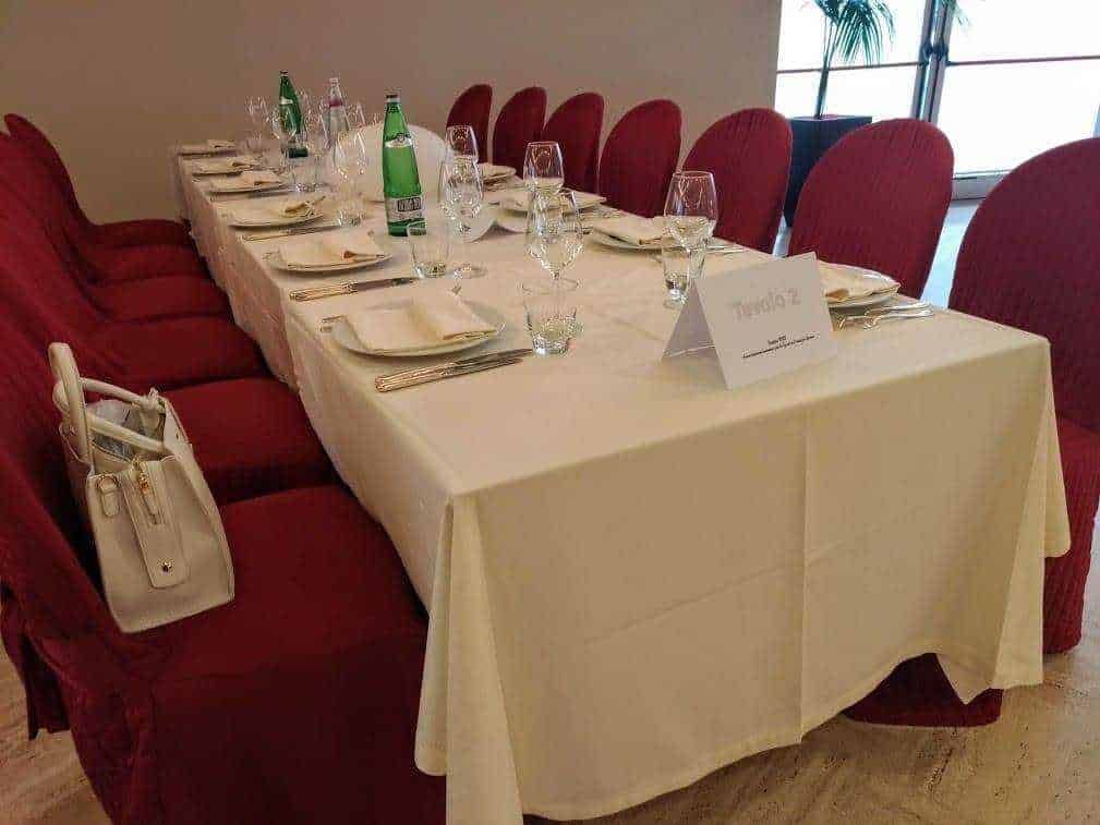 Tavolo per riunioni con tovaglia bianca, sedie rosse, bicchieri da vino e bottiglie di acqua in un ambiente elegante e professionale. Ideale per incontri di lavoro e cene di gruppo.