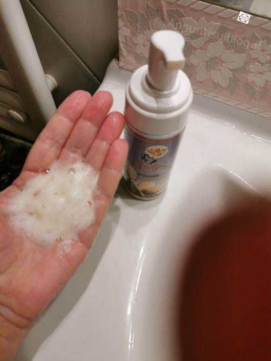 Schiuma detergente in mano vicino a boccetta di sapone liquido sul lavandino.