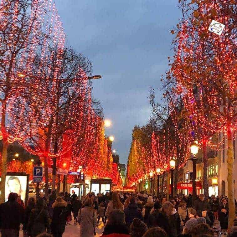 Vetrine di luci natalizie illuminate lungo una strada cittadina con persone che passeggiano, creando un'atmosfera festiva e accogliente durante le festività invernali.