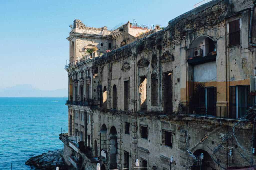 Vecchio edificio sul mare in stile mediterraneo con pareti corrosi e finestre, vista panoramica sulla costa e il mare azzurro, simboleggia l'arte e la storia di un paesaggio costiero italiano.