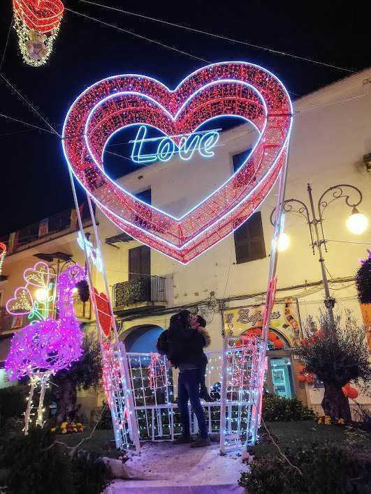 Cervo di luci a forma di cuore con la parola "Love" luminosa, decorazioni natalizie in un centro urbano di sera, atmosfera romantica e festiva, illuminazioni colorate per occasioni speciali.