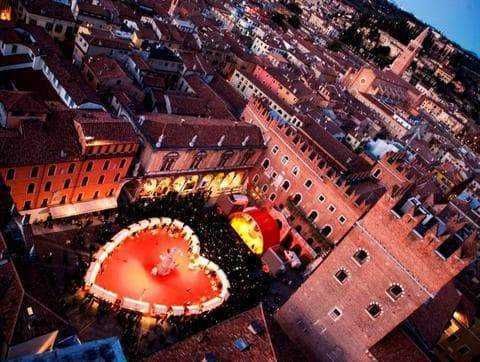 Corte antica con cuore di luci rosse e decorazioni natalizie, vista panoramica di Bologna, atmosfera romantica e suggestiva con edifici storici e tunnel illuminati.
