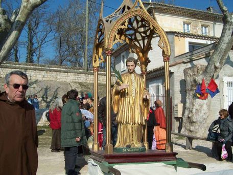 San Valentino storia e 12 tradizioni insolite nel mondo 6 Calco in legno di San Valentino durante una festa religiosa all'aperto con partecipanti e decorazioni, in un cortile di paese con case storiche e alberi nudi, giornata di sole.