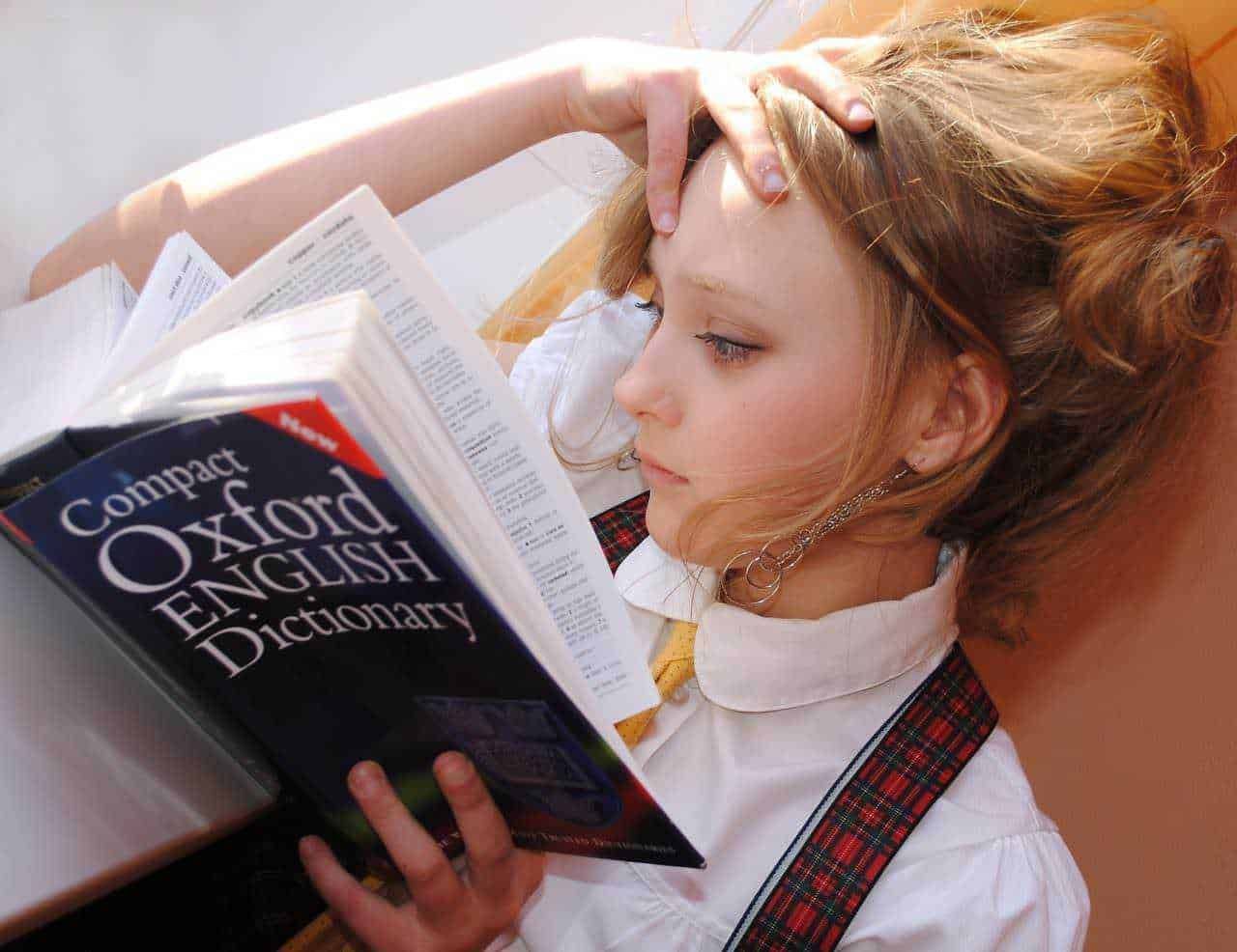 Viaggiare senza parlare inglese: Oxford English Dictionary in mano a giovane studentessa che studia e impara l'inglese, concentrata sulla lettura e sull'apprendimento linguistico efficace, con focus sulla crescita personale e l'educazione.