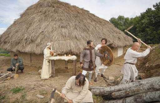 Vita quotidiana nell'antica civiltà, persone in abiti storici che lavorano e praticano attività tradizionali davanti a una capanna di paglia.