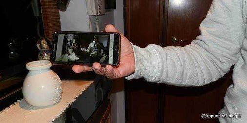 Come evitare i furti in casa in vacanza con un timer temporizzatore 5 Ripresa di una mano che tiene uno smartphone con schermo acceso, inquadrando una scena di una conversazione o video alla luce di una lampada d'ambiente.