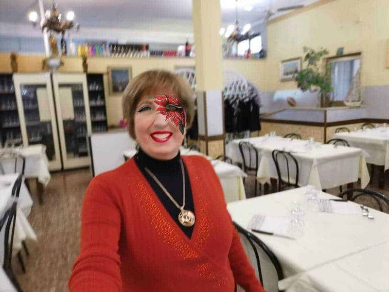 A1: donna sorridente con trucco artistico e abbigliamento natalizio in un ristorante elegante.