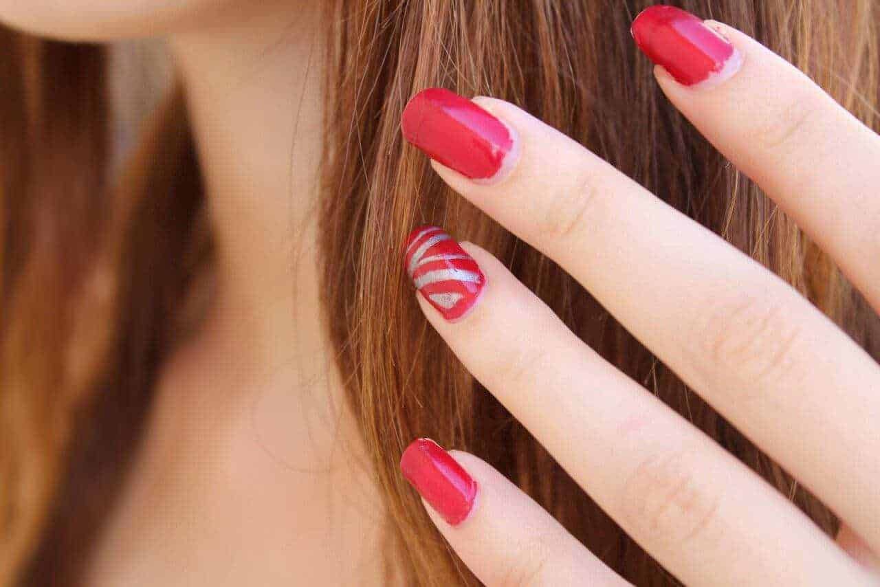 Unghie decorate con smalto rosso e dettagli a righe bianche e rosse, manicure elegante e alla moda.