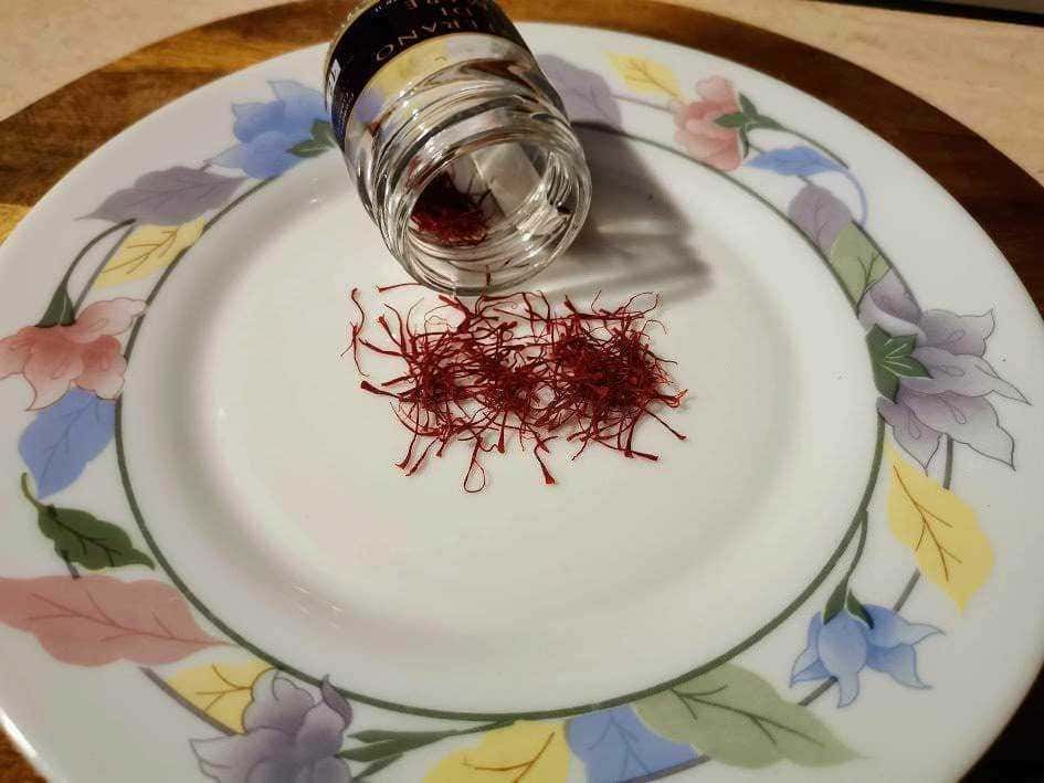 Fiocchi di zafferano con contenitore di spezie su piatto decorativo, ingrediente essenziale per cucina gourmet, perfetto per ricette tradizionali e sofisticate.