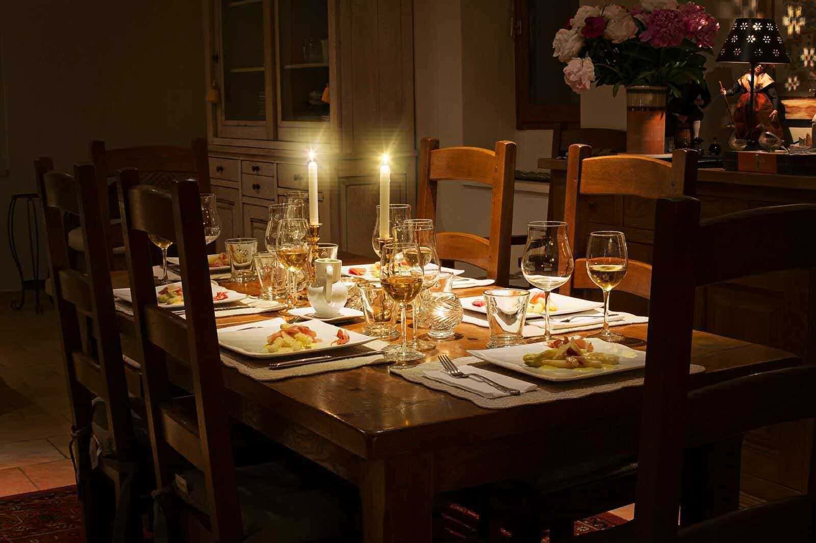 Ricetta tavola imbandita elegantemente con candela accesa, bicchieri di vino e piatti di antipasti, atmosfera calda e intima in una sala da pranzo rustica e accogliente.