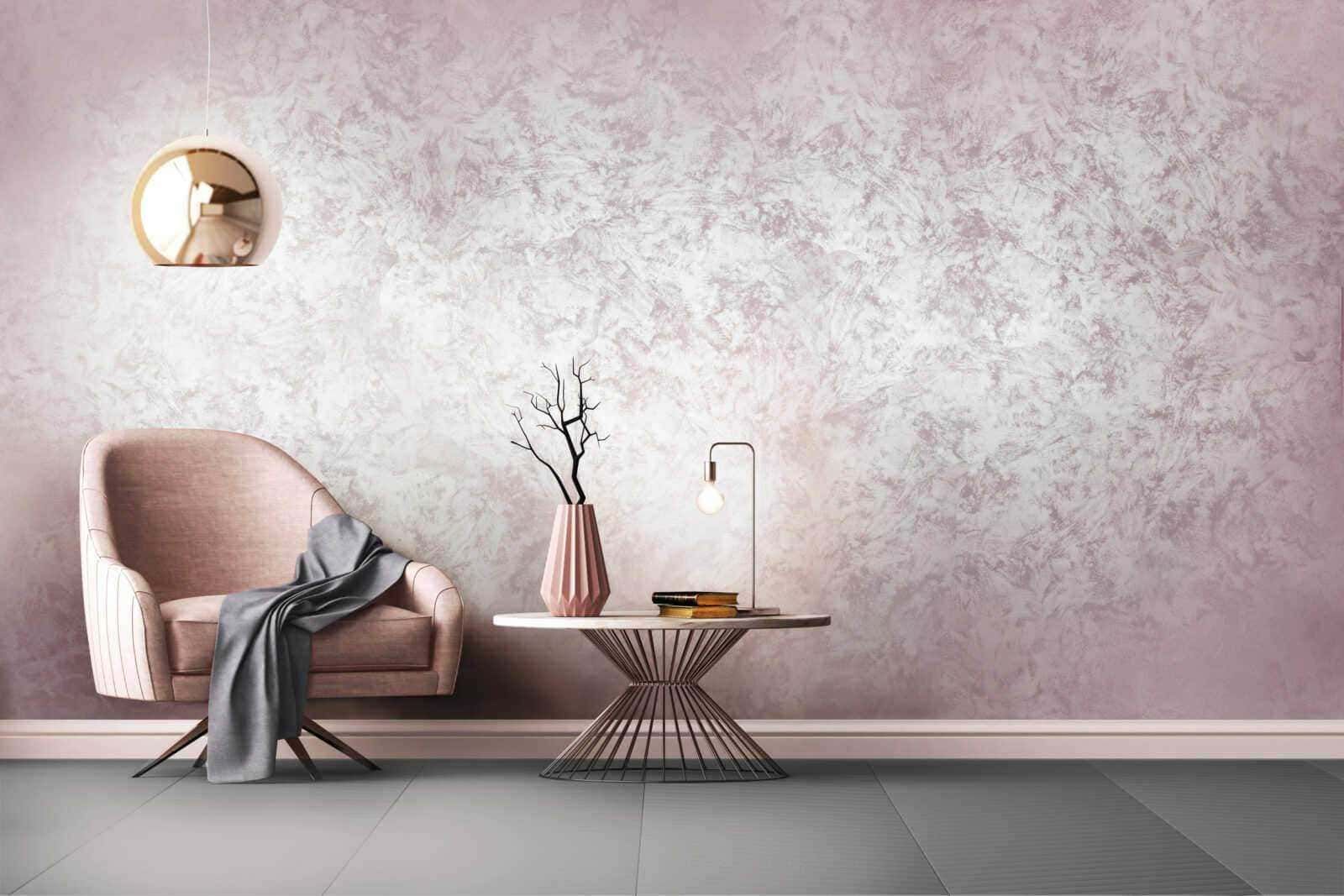 Elegante zona living con poltrona rosa, tavolino decorativo con lampada e vaso con ramo secco, parete rosa con texture sofisticata, design moderno e raffinato, ideale per arredo interno di stile contemporaneo.