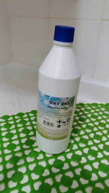 Oxy Del disinfettante attivo per igiene domestica e ambienti, bottiglia da 1 litro su piastra verde con pattern a quadratini bianchi e sfondo bianco.
