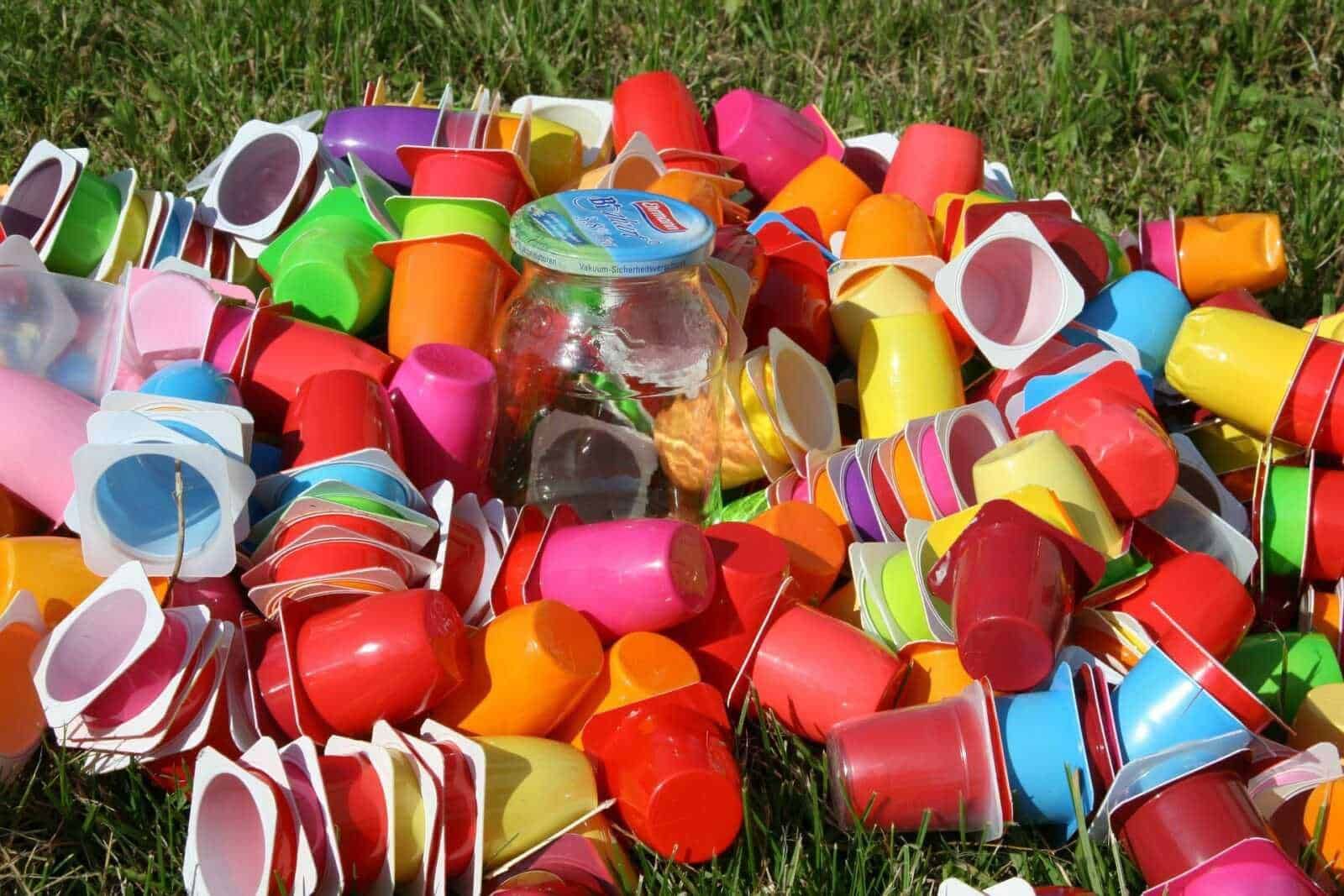 Colorati bicchieri di plastica abbandonati su erba, simbolo di spreco e rifiuti ambientali.