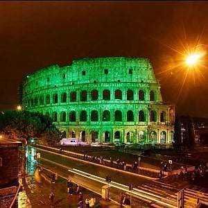 Maestoso Colosseo illuminato di verde di sera, simbolo iconico di Roma e meta turistica mondiale, con luci che evidenziano le sue arcate storiche in una notte vivace.