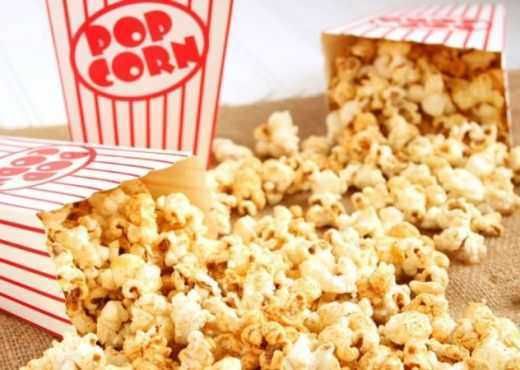 Popcorn in sacchetti di carta con chicchi di popcorn sparsi, snack pop corn croccante e gustoso. Immagine perfetta per articoli su snack, cinema, intrattenimento e ricette di popcorn.