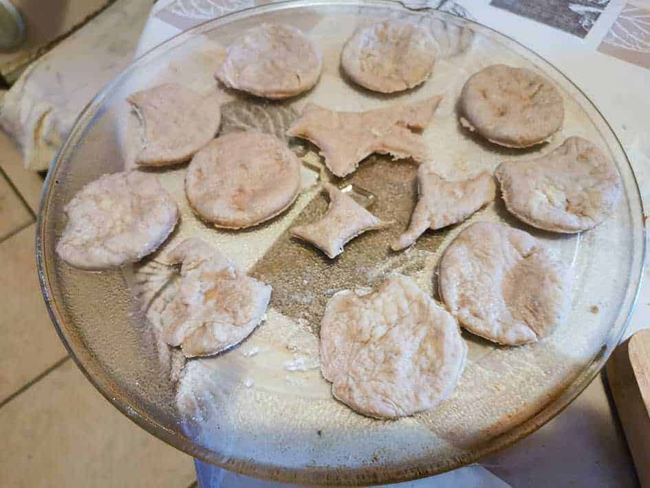 Frollini fatti in casa con farina e zucchero, pronti per essere infornati, su un vassoio di vetro.